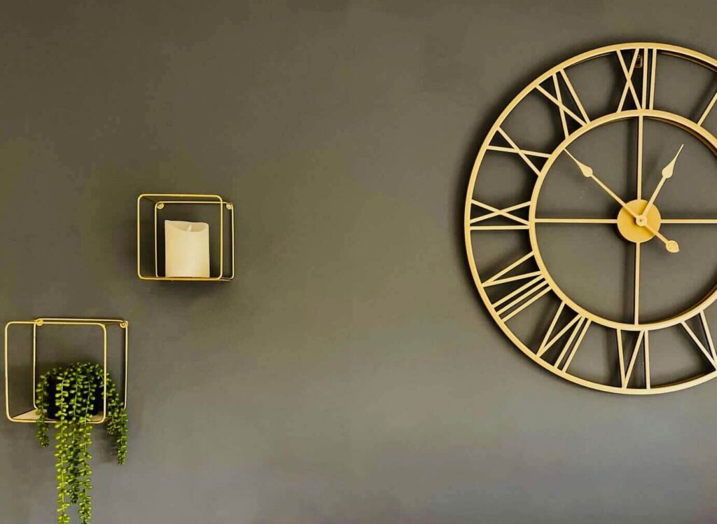 a large gold clock and gold floating shelves on a grey wall