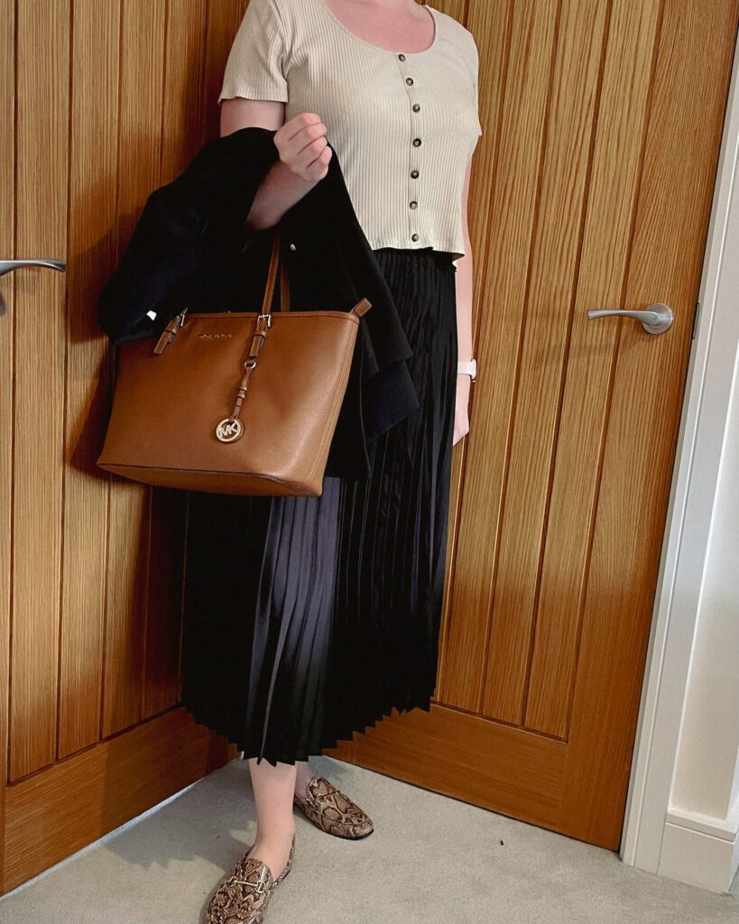 a girl wearing a nude crop top and black midi skirt with a brown bag